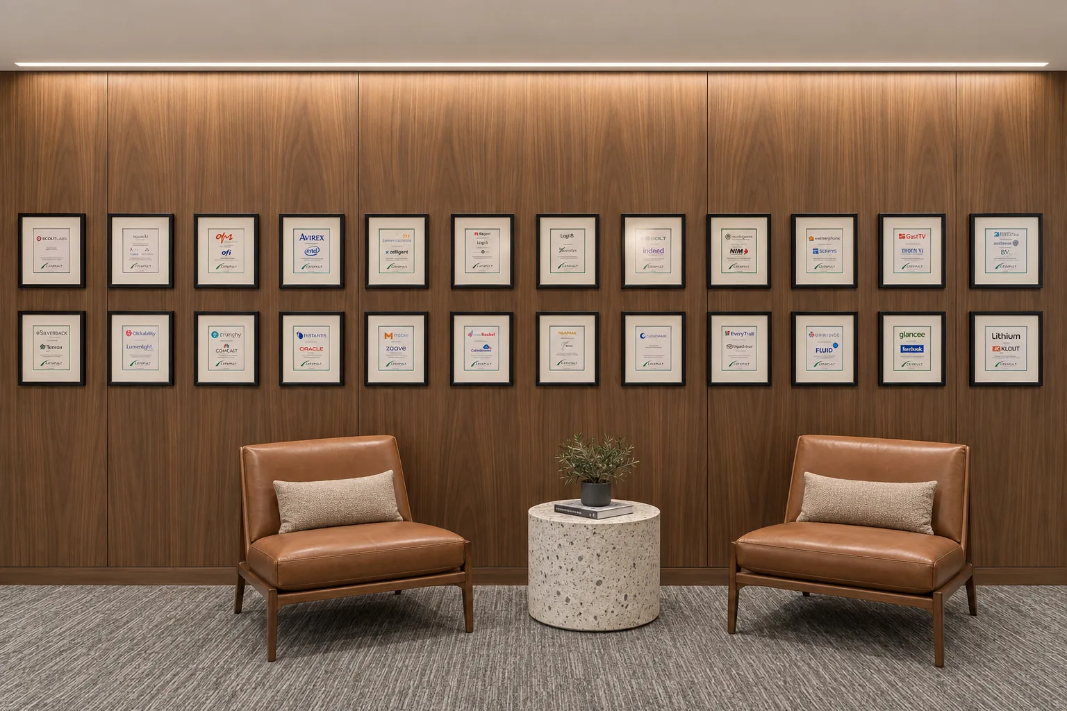 Two rows of framed transaction tombstones on a walnut wall above two leather lounge chairs